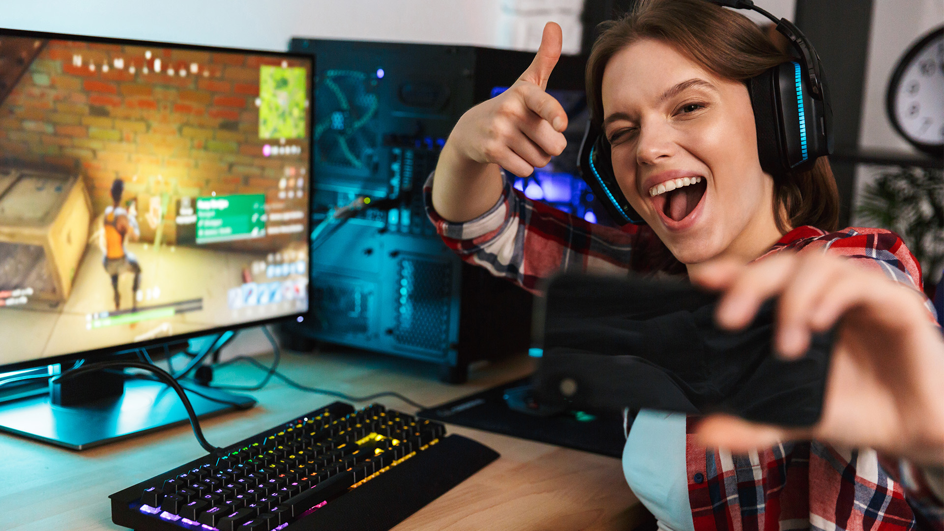 A woman takes a selfie in front of a gaming computer running Fortnite. 